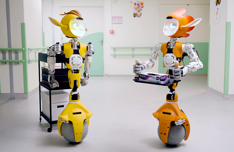 Two Mirokai robots move through a hospital hallway.